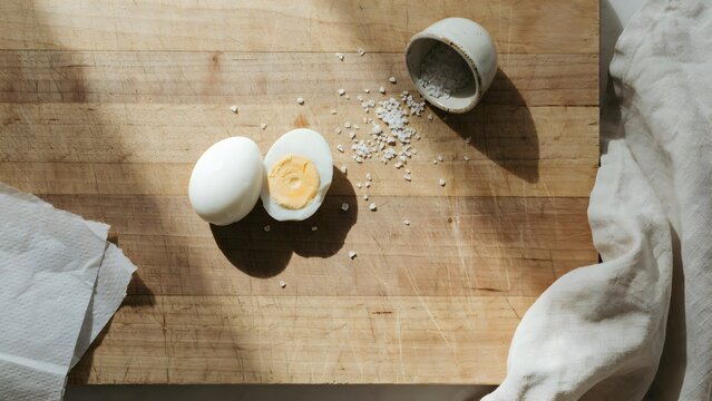 Freshly cracked hard-boiled eggs on wooden cutting board with salt and spoon