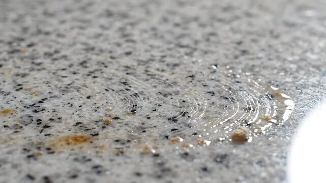 Spilled Liquid Being Wiped Clean From a Granite Countertop with a White Cloth, Demonstrating Cleaning and Surface Care.