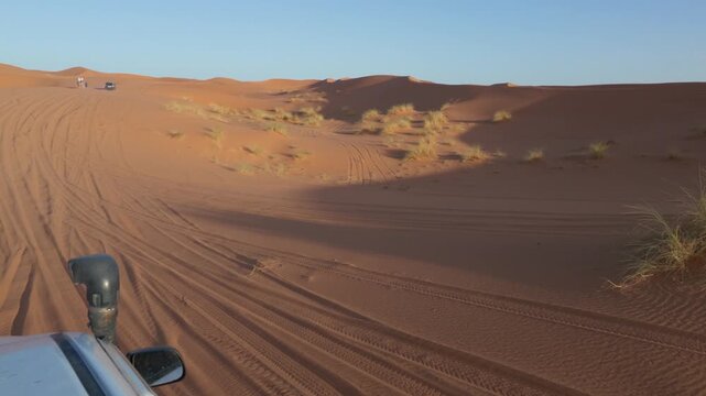 Off-road vehicle driving through vast sand dunes on a desert safari adventure, leaving tire tracks on the orange sand during a sunny day with clear blue sky in the sahara