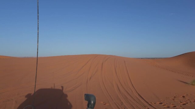First person view from an off road vehicle driving on the vast and scenic red sand dunes of the sahara desert, showing the car's snorkel and antenna under a clear blue sky