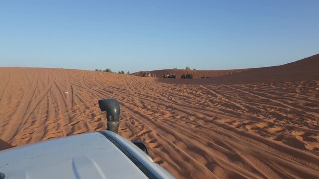 Point of view shot from a 4x4 off road vehicle driving through red sand dunes during an exciting desert safari and arriving at a traditional bedouin camp for tourists