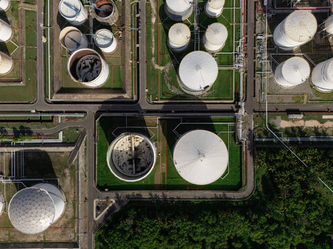 Aerial view of industrial oil storage tanks with white circular structures, pipeline networks, and surrounding green vegetation in Bajos de Haina, San Cristobal Province, Dominican Republic.