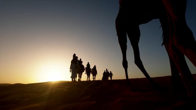Silhouette of a camel caravan with nomads crossing the sahara desert dunes at sunset, embodying a journey of adventure, trade, and traditional desert transportation