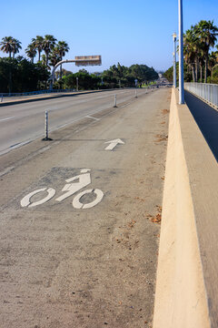 A dedicated bicycle lane on a coastal bridge or roadway featuring a white stenciled bike symbol and directional arrow, San Diego, California