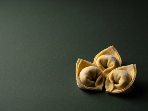 Small pile of stuffed Italian tortellini cappelletti pasta dumplings displayed on dark textured elegant surface