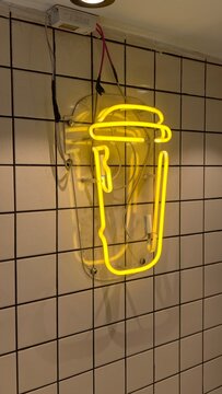 Neon sign illuminating a tiled wall, glowing bright yellow, symbolizing coffee, tea, and beverage businesses, promoting drinks, cafes, and snack bars with a modern aesthetic