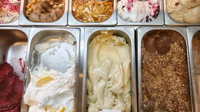 Displaying a variety of artisanal Italian gelato flavors in metal containers, showcasing creamy textures and tempting toppings for a sweet dessert experience