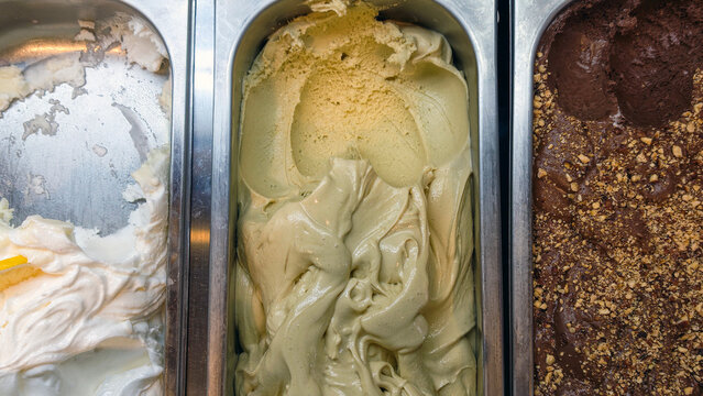 Displaying three flavors of artisanal gelato in a stainless steel freezer, offering a refreshing sweet treat for summer desserts, dairy products, and menu concepts