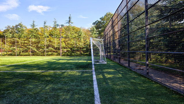 Artificial turf football field waiting for players, symbolizing sports, fitness, and outdoor recreation, with goal and protective fencing under a clear sky