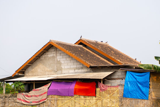 Rural Asian home with colourful clothes drying on bamboo fence under grey sky