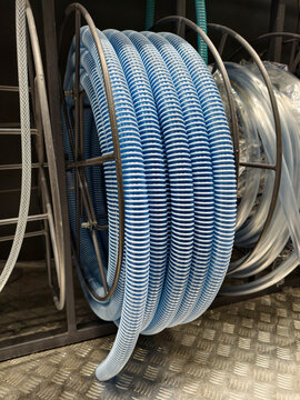 Blue corrugated hose coiled and stacked is shown in a retail construction environment for customer selection and purchase