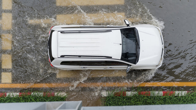 Aerial view of a white SUV driving through a flooded city street during heavy seasonal rainfall