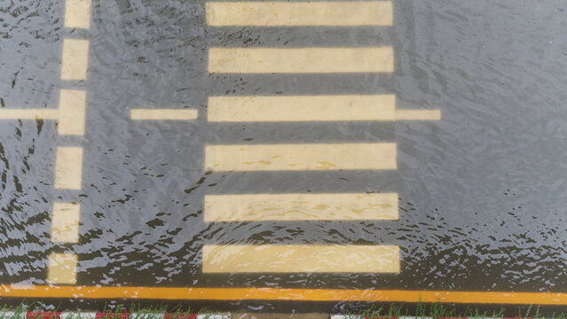 Aerial view of a flooded pedestrian crosswalk on an asphalt road during heavy rainfall weather