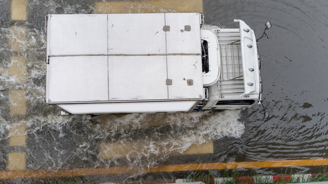 Aerial view of a white delivery truck driving through a flooded city street after heavy rainfall