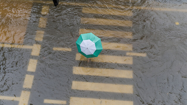 Aerial view of a person walking through a flooded city street crossing with a green umbrella