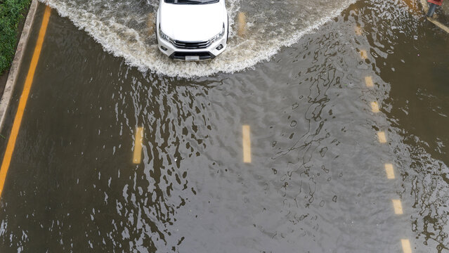 White vehicle driving through deep flood water on a city street after heavy tropical rainfall