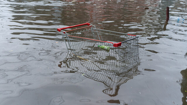 A metal shopping cart abandoned in a flooded city street after heavy rain and storm conditions