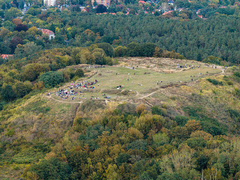 Aerial view of Drachenberg hill with people relaxing on the grassy summit surrounded by dense forest and urban landscape in Berlin, Berlin, Germany.