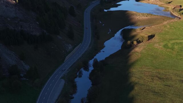 Aerial view of Lake Sils and winding road with cars driving through the mountainous landscape of Maloja District, Grisons, Switzerland.