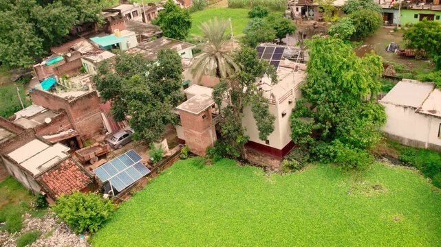 Aerial view of solar panels installed on rooftops in a rural village setting with lush green fields and traditional houses in Lucknow, Uttar Pradesh, India.