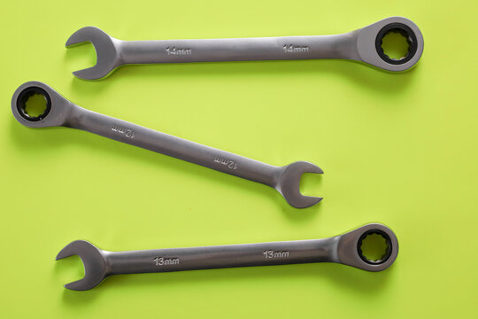 Three steel combination ratchet wrenches in sizes 12, 13, and 14 mm are neatly arranged on a bright lime green background. The composition perfectly illustrates high-quality hand tools for auto repair