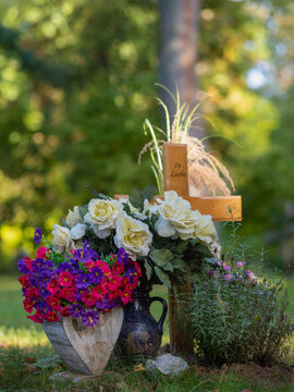 Holzkreuz ohne Namen mit k&uuml;nstlichen Blumen am kleinen Baum Urnengrab auf dem Waldfriedhof
