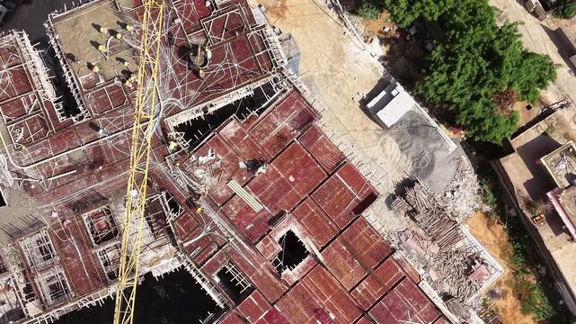 Aerial view of construction site with workers pouring concrete slab and operating crane in India.