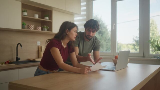 Couple reviewing finances and bills at kitchen table with laptop and calculator, home budgeting and financial planning