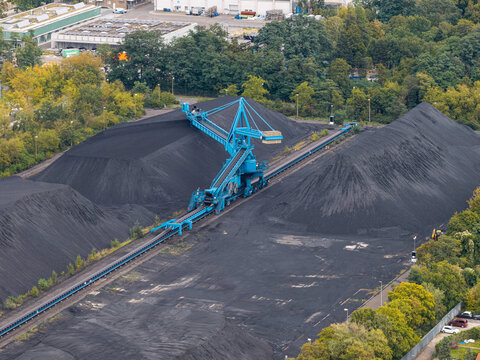 Aerial view of a large blue stacker machine operating on massive piles of coal in an industrial mining area in Berlin, Berlin, Germany.