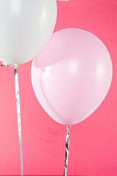 Close-up of two pink and white helium filled balloons against a pink background 