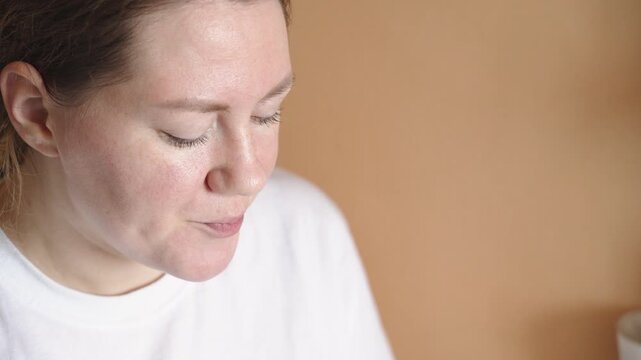 Woman drinks freshly brewed tea from large transparent cup in peaceful home atmosphere, portrait closeup. Calm enjoyment of aromatic invigorating green tea brewed from dry petals.