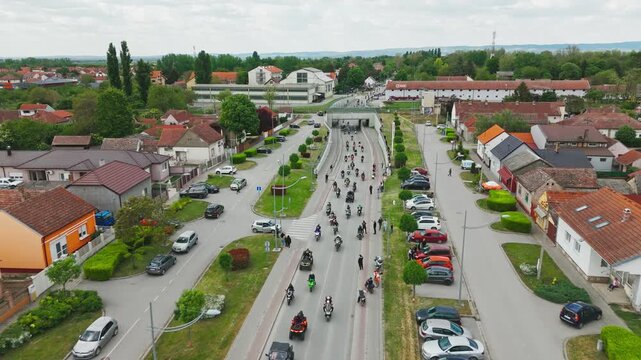 Aerial view of a motorcycle rally procession moving through an urban underpass surrounded by houses and parked cars in Sremska Mitrovica, Vojvodina, Serbia.