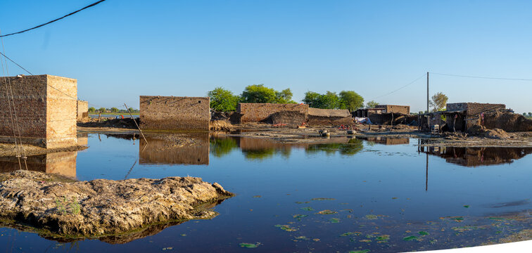 View of flooded rural landscape with partially submerged brick houses and calm water reflecting the clear blue sky in Jacobabad, Sindh, Pakistan.