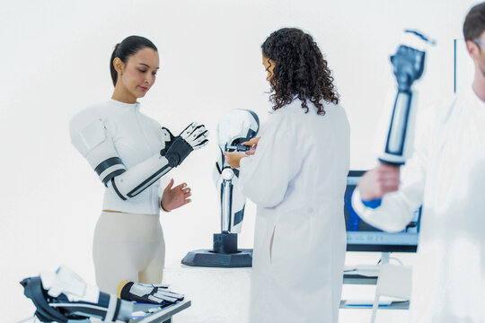 Sensor driven robotics research: a test wearer brings the mechanical fingers of her robotic forearm close to a bench manipulator so the two sensor sets can be compared