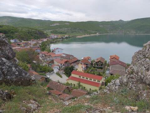 View of the village of Lin with its traditional red-tiled roofs and a prominent church situated on the shores of Lake Ohrid, surrounded by green hills in Lin, Korce County, Albania.