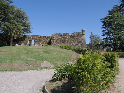 View of the historic stone walls and watchtower of Castelo do Castro surrounded by lush green lawns and trees under a clear blue sky in Vigo, Pontevedra, Spain.