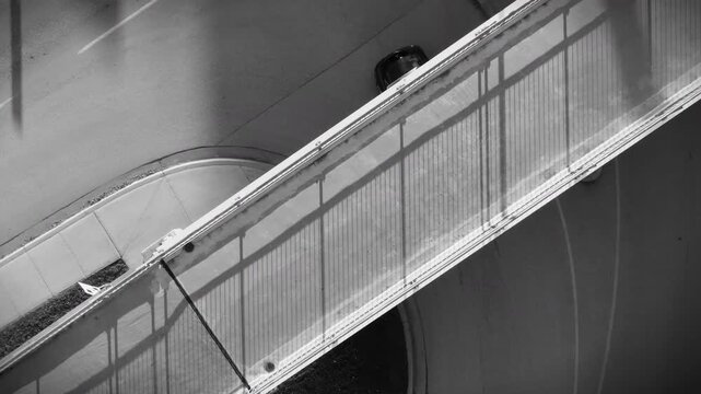 Overhead view in black and white of a pedestrian overpass with cars driving and turning around a corner underneath.