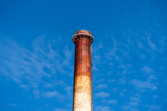 View of a tall, weathered industrial chimney with rust-colored textures against a bright blue sky in Poland.