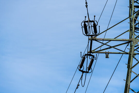 View of a high-voltage electricity pylon with insulators and power lines set against a clear blue sky in Poland.
