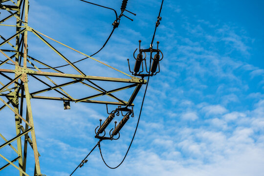 View of a high-voltage electricity pylon with insulators and power lines against a clear blue sky in Poland.
