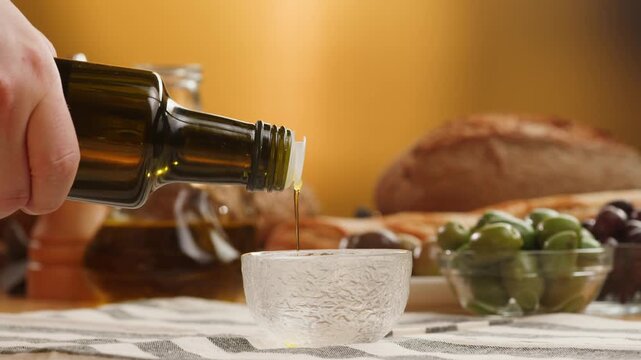 Olive oil pouring close up, extra virgin olive oil flowing from glass bottle and jug into bowl, golden oil for Italian and Spanish Mediterranean cuisine