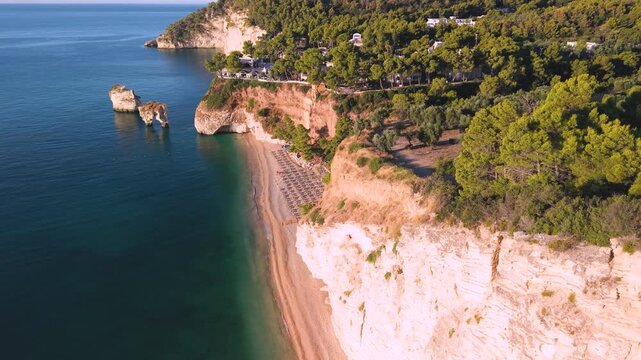 Baia delle Zagare morning light on pink sand and iconic vertical sea stack, drone flyby down to empty beach in luxury resort, Gargano Puglia Italy. 4K cinematic Adriatic coast