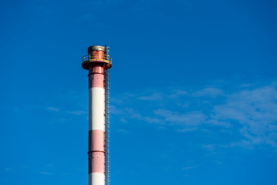 View of a red and white striped industrial smokestack with a ladder against a clear blue sky in Poland.