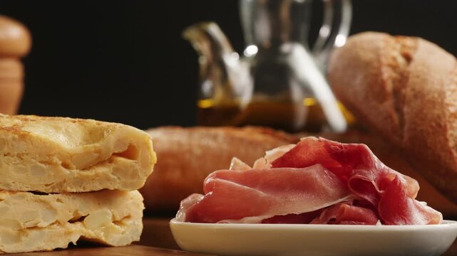 Spanish omelette with jamon serrano, tortilla and iberico cured ham appetizer on wooden table, traditional Spanish breakfast close up in cafe
