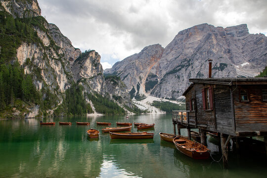 View of wooden boats floating on the emerald waters of Lago di Braies with a rustic wooden boathouse on stilts and the towering peaks of the Dolomites in the background, Braies, Veneto, Italy.