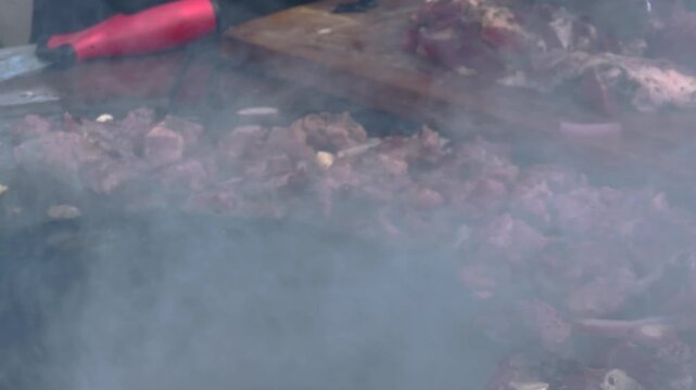 Juicy seasoned pork meat steaks and onions grilling on hot flat iron barbecue plate surrounded by dense white aromatic smoke during an outdoor culinary cooking event. 4K video.