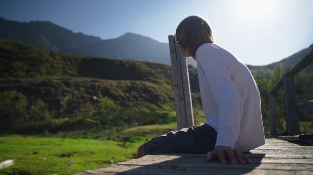 Teenager sit quietly on wooden bridge beside flowing stream, taking peaceful moment alone in natural landscape, illustrating mindfulness, emotional wellbeing, self-reflection,connection with nature