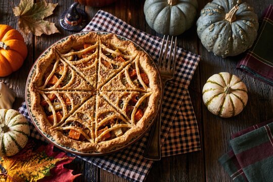 Pumpkin pie with jack-o-lantern face cut into crust, Halloween overhead flat lay with pumpkins and gingham napkin