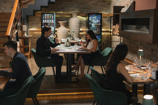 Handsome couple in a luxury restaurant, a beautiful Asian woman and her partner drinking white wine poured by a waiter.