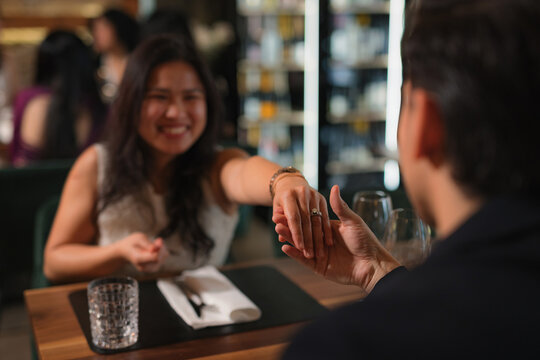 Emotional marriage proposal at a restaurant, a man giving an engagement ring to a smiling, surprised Asian woman.